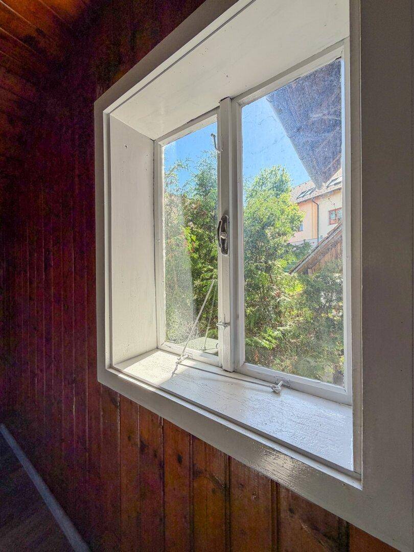 Nahaufnahme eines Fensters in einem Dachzimmer mit Holzverkleidung, das den Blick ins Grüne freigibt.