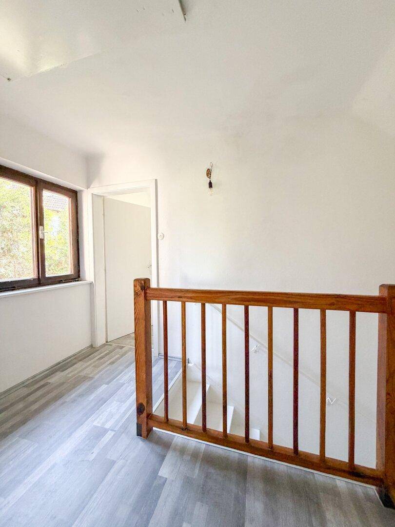 Heller Treppenabsatz mit Holzgeländer, Laminatboden und einem Fenster, das Tageslicht spendet.