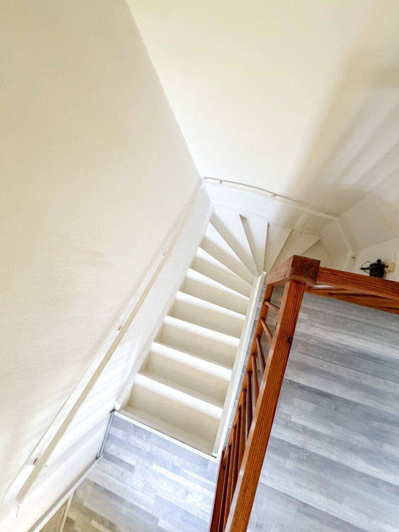 Treppenhaus mit weiß gestrichenen Stufen und einem Holzgeländer, das in die obere Etage führt.