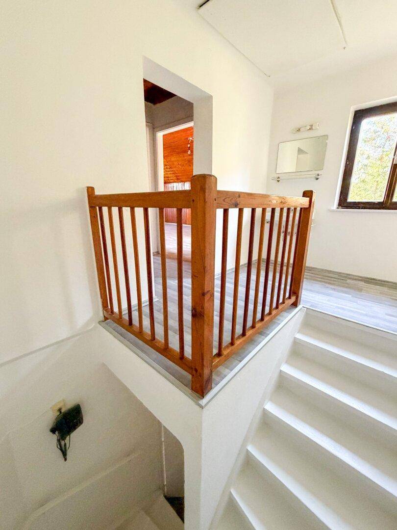 Heller Treppenabsatz mit Holzgeländer und Laminatboden, der zu weiteren Räumen führt.