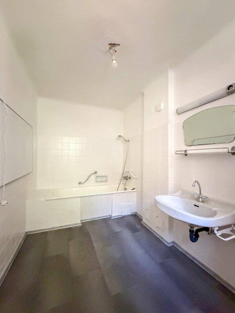 Badezimmer mit Badewanne, Waschbecken und weißen Fliesen, ausgestattet mit einem Spiegel.