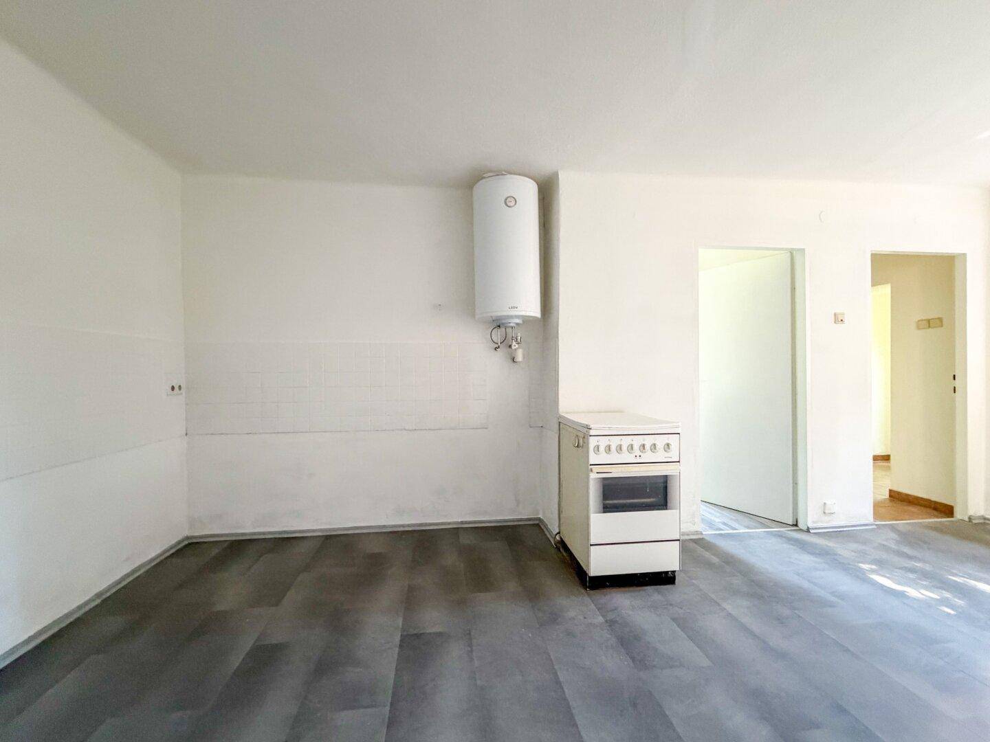 Leere Küche mit Laminatboden, einem Boiler und einem freistehenden Herd, bereit für die Gestaltung.