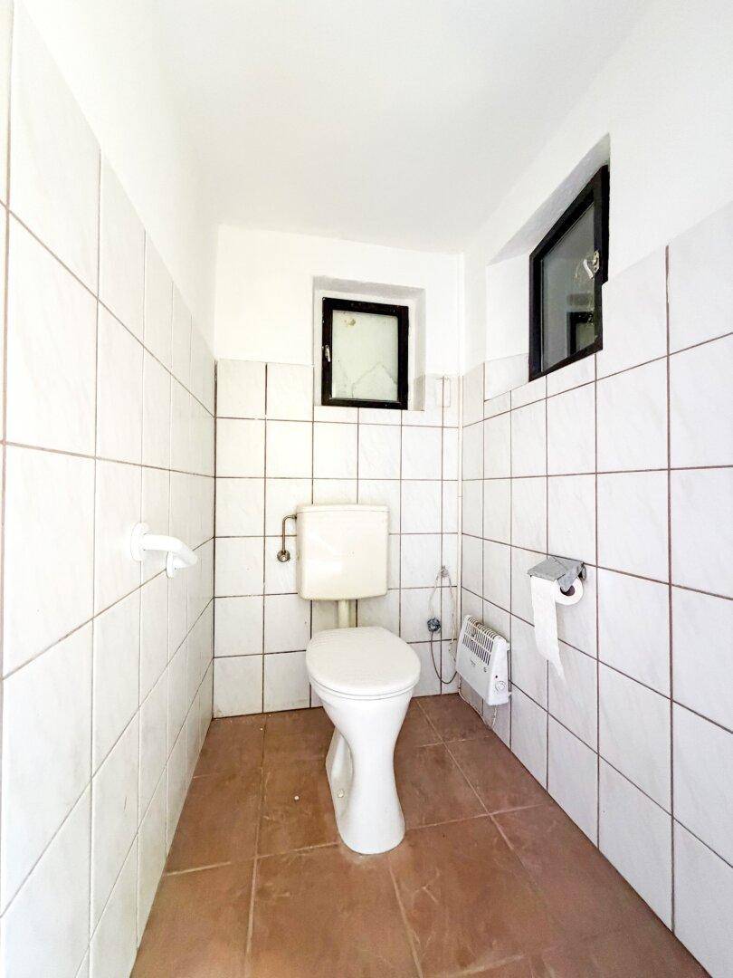 Kleines WC mit weißen Fliesen an den Wänden und einem Fenster für natürliche Belüftung.