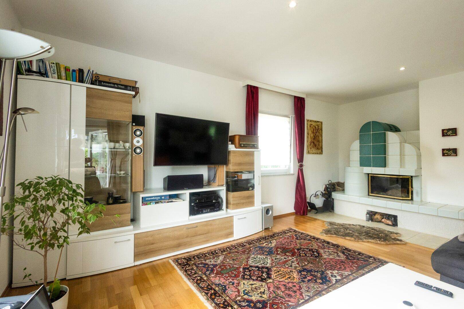 Wohnzimmer mit Holzboden, Fernsehmöbel und einem traditionellen Kachelofen.