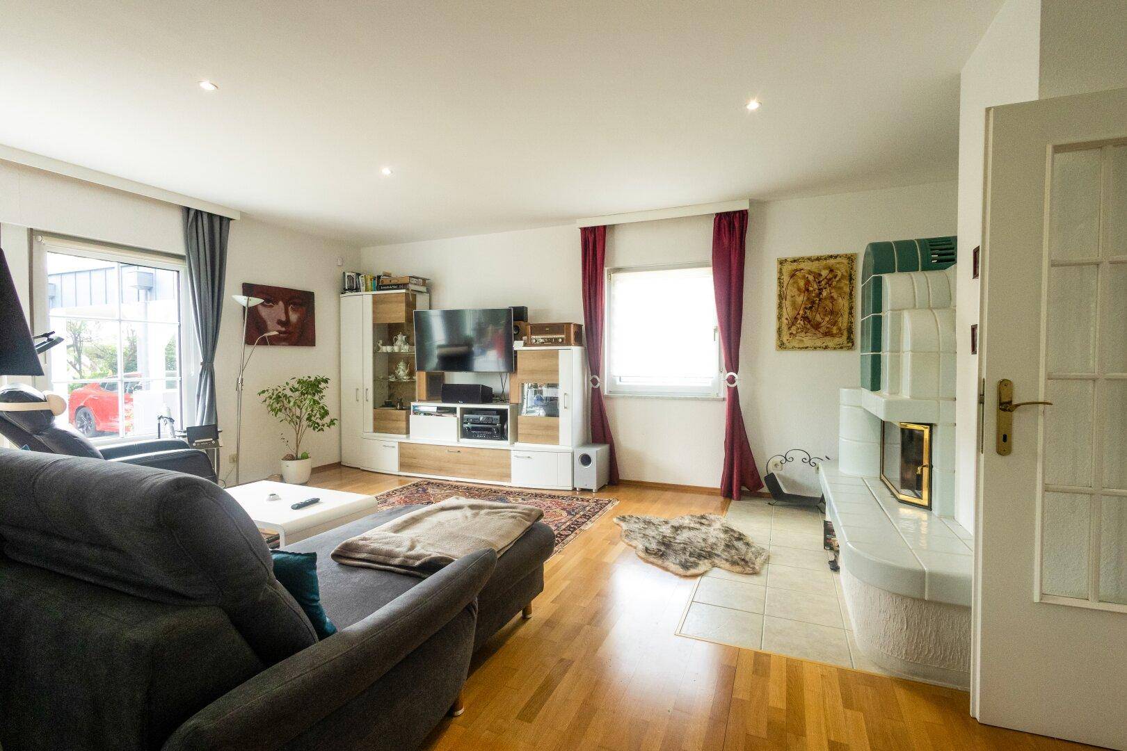 Geräumiges Wohnzimmer mit Kachelofen, Sofa und Zugang zu anderen Räumen.