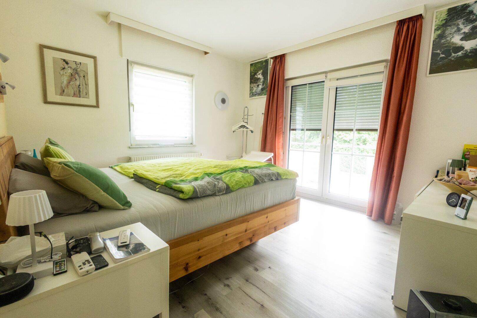 Helles Schlafzimmer mit Holzbett, Laminatboden und Zugang zum Balkon.