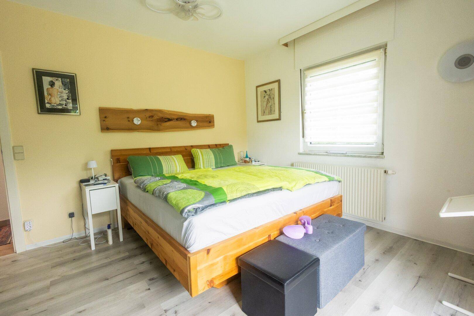 Gemütliches Schlafzimmer mit Holzbett, Laminatboden und gelber Akzentwand.