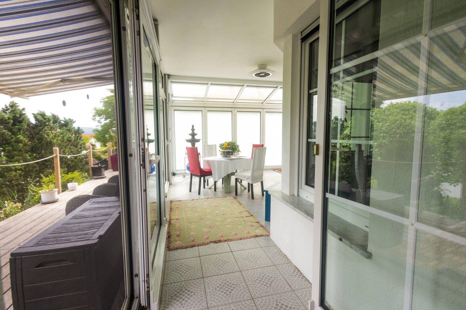 Heller Wintergarten mit Essbereich, großen Fenstern und Zugang zur Terrasse.