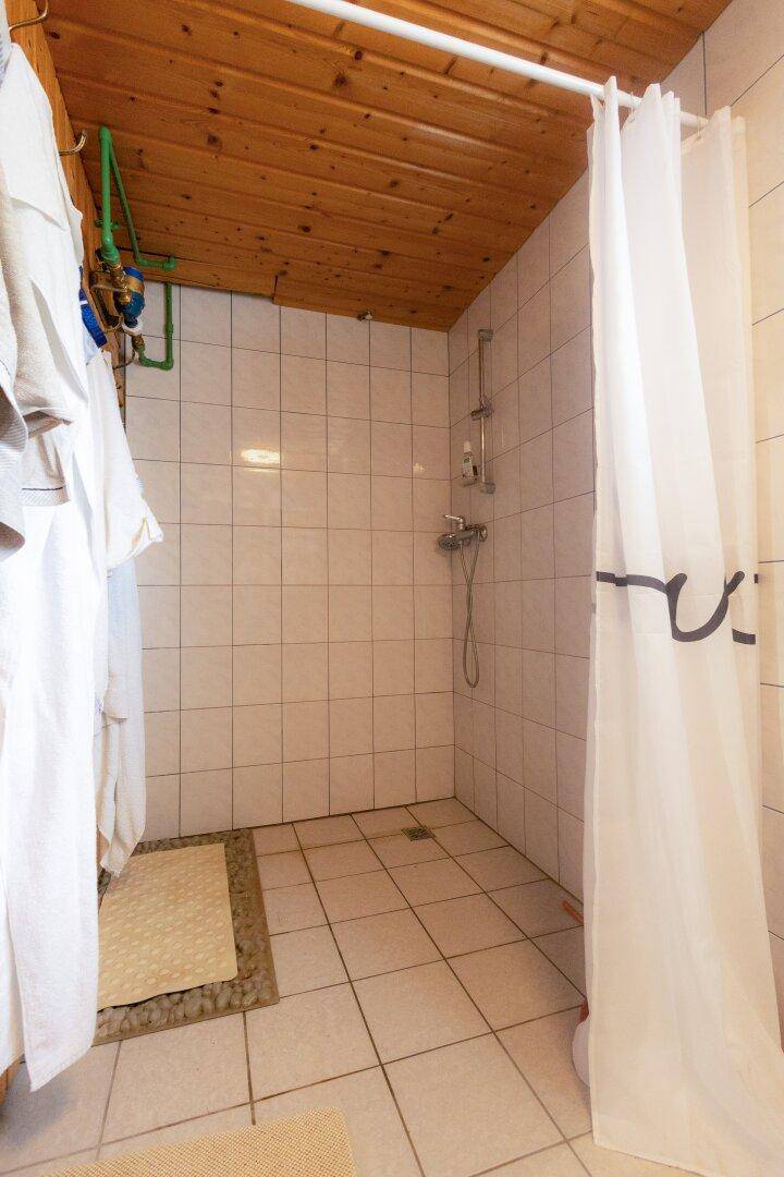 Einfache Duschkabine mit weißen Fliesen und Holzdecke in einem Badezimmer.
