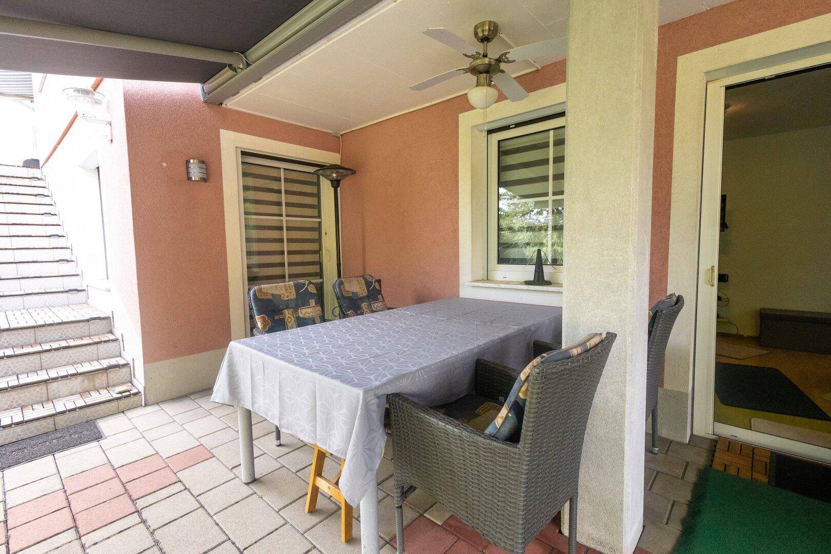 Überdachte Terrasse mit Esstisch, Stühlen und Deckenventilator für Mahlzeiten im Freien.