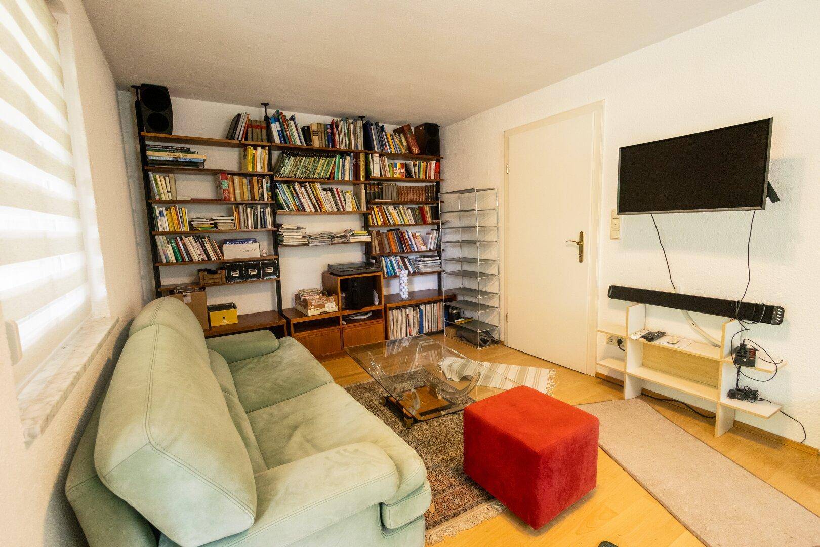 Wohnzimmer mit großem Bücherregal, bequemer Couch und Fernseher.