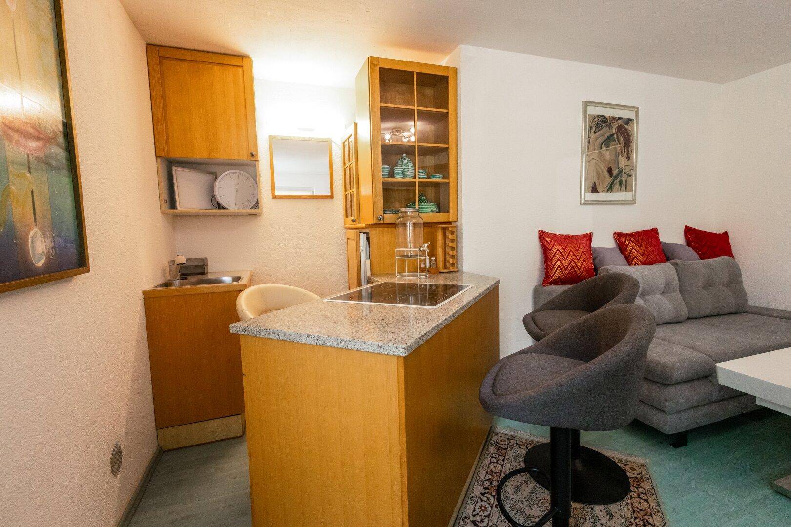 Kleine Küchenzeile mit Granit-Arbeitsplatte, Barhockern und integriertem Kochfeld.