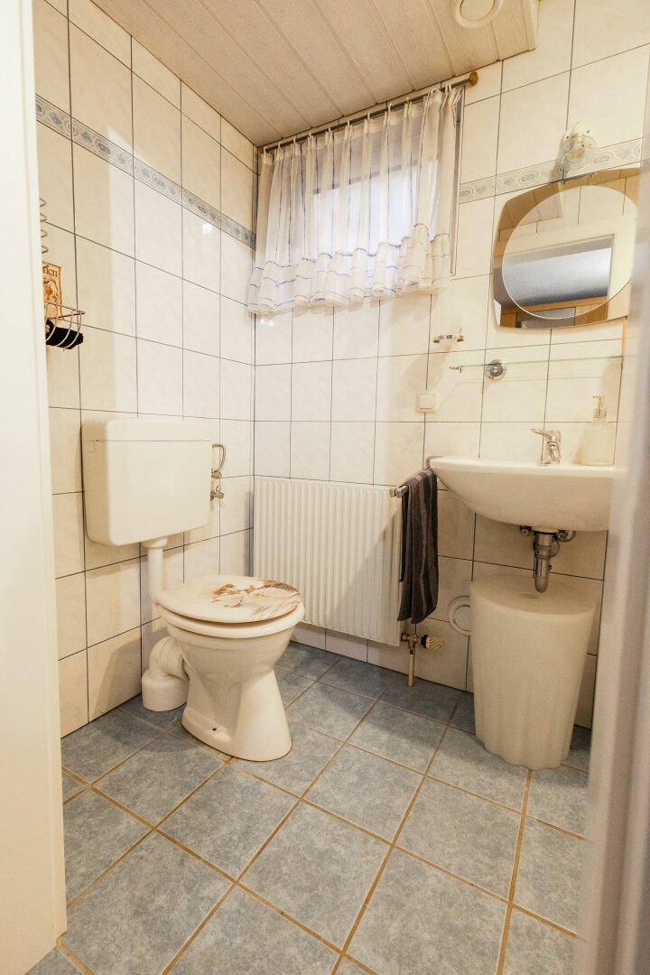 Kleines Gäste-WC mit Fenster, Toilette und Waschbecken in hellen Fliesen.