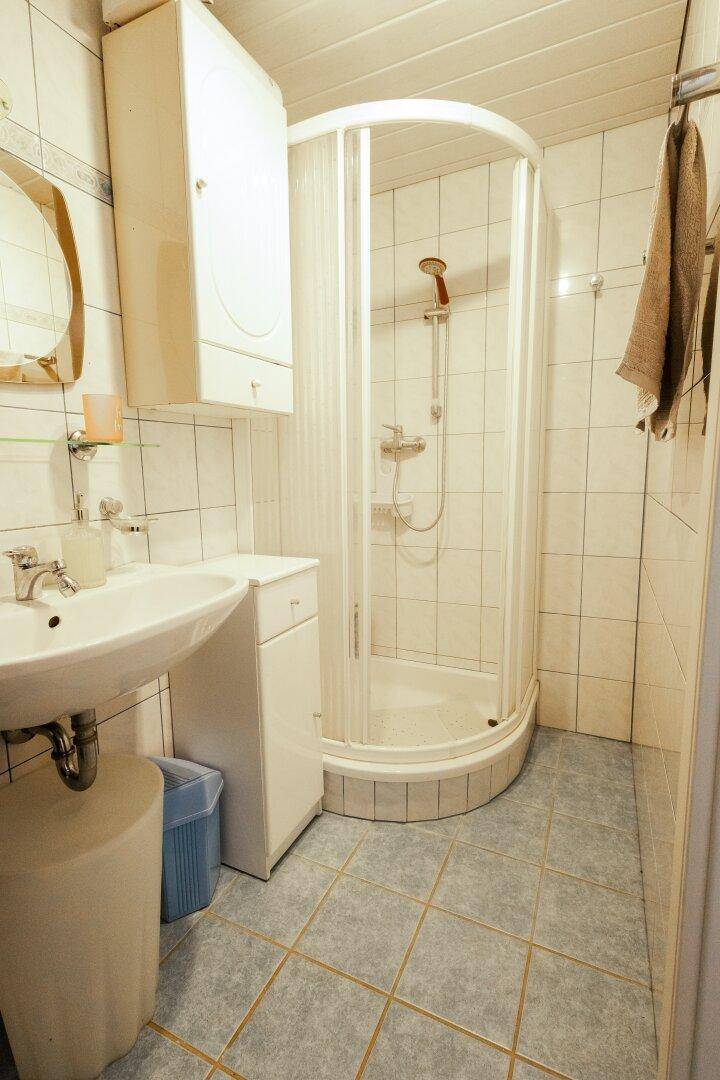 Badezimmer mit Duschkabine, Waschbecken und Spiegelschrank in hellen Fliesen.