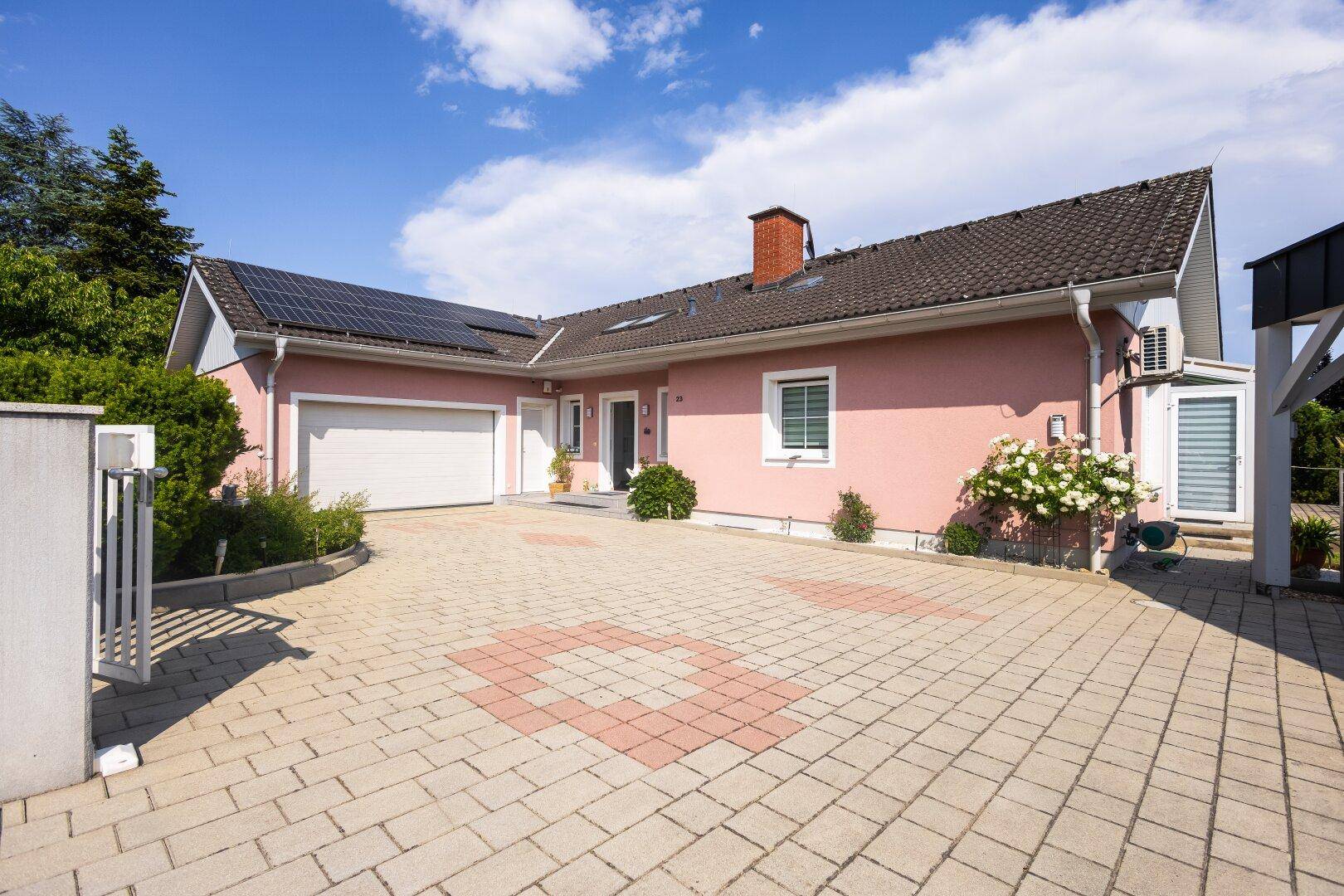 Vorderansicht des Hauses mit gepflasterter Einfahrt, Garage und Solaranlagen.