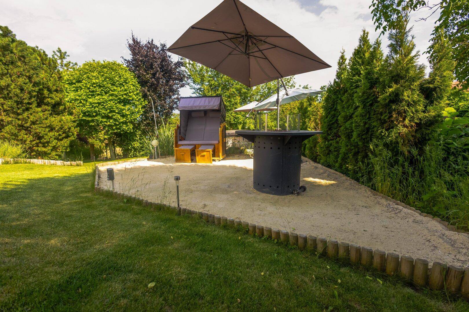 Gemütlicher Gartenbereich mit Sandfläche, Strandkorb und Sonnenschirm.