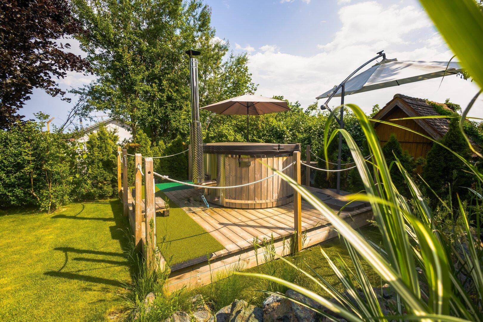Entspannungsbereich im Garten mit Holzdeck, Hot Tub und Sonnenschirm.