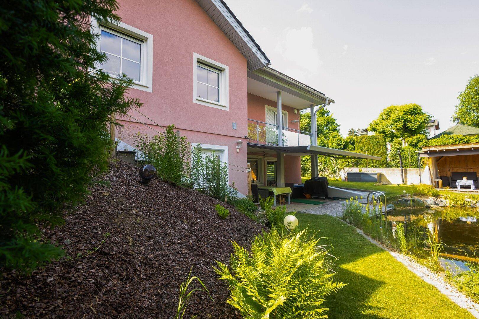 Seitenansicht des Hauses mit Garten, Teich und üppiger Bepflanzung.