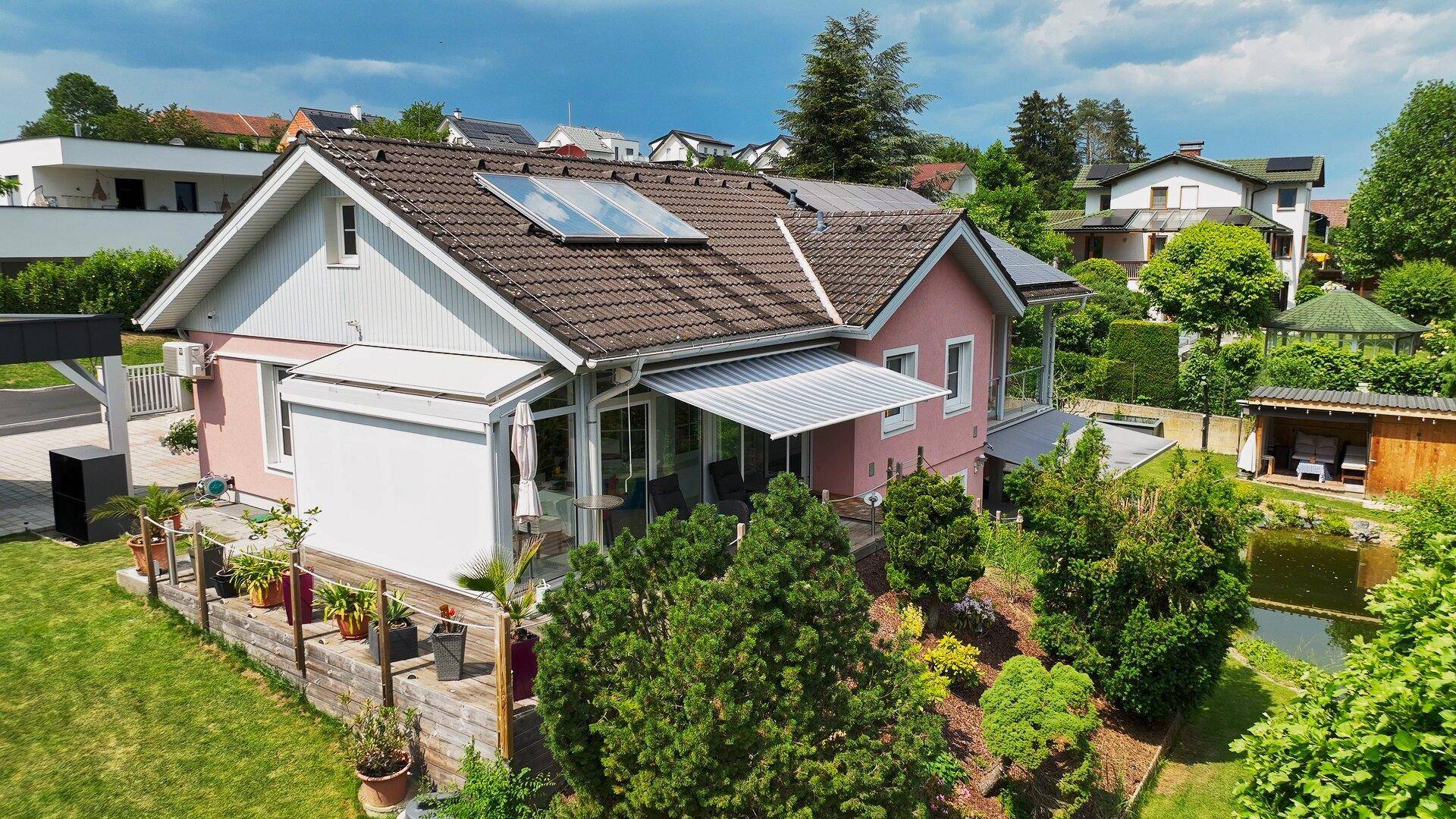 Seitenansicht des Hauses mit Garten, Teich, Solaranlagen und Terrasse.