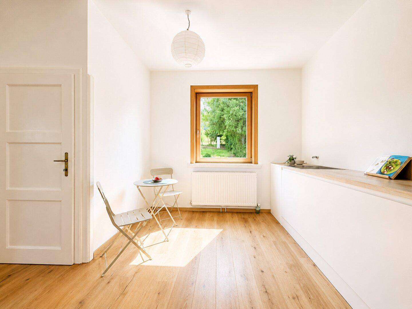 Helle Küche mit Holzboden, Fenster und Platz für einen kleinen Esstisch.