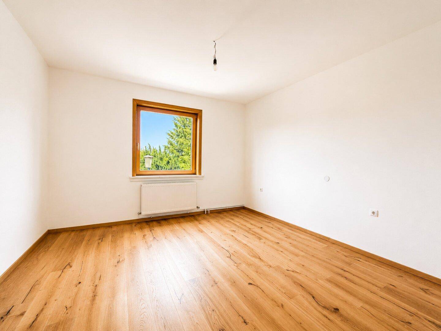 Geräumiges Schlafzimmer mit Holzboden, weiß gestrichenen Wänden und großem Fenster.