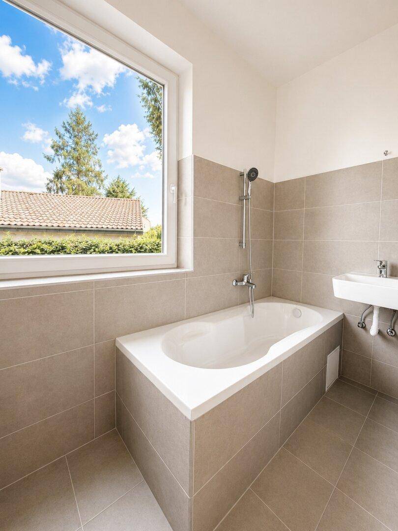 Modernes Badezimmer mit beigen Fliesen, Badewanne und großem Fenster mit Ausblick.