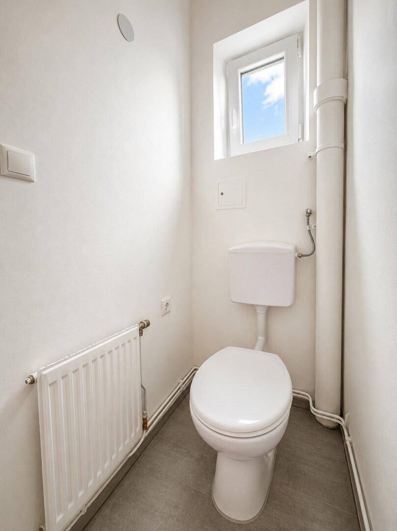 Separates WC mit Fenster, weißer Toilette und Heizkörper.