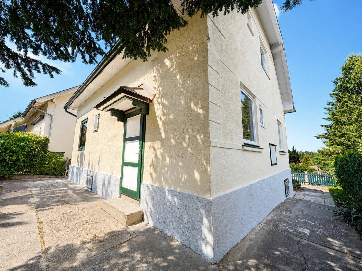 Seitenansicht des Hauses mit hellem Putz, grüner Eingangstür und gepflegtem Außenbereich.