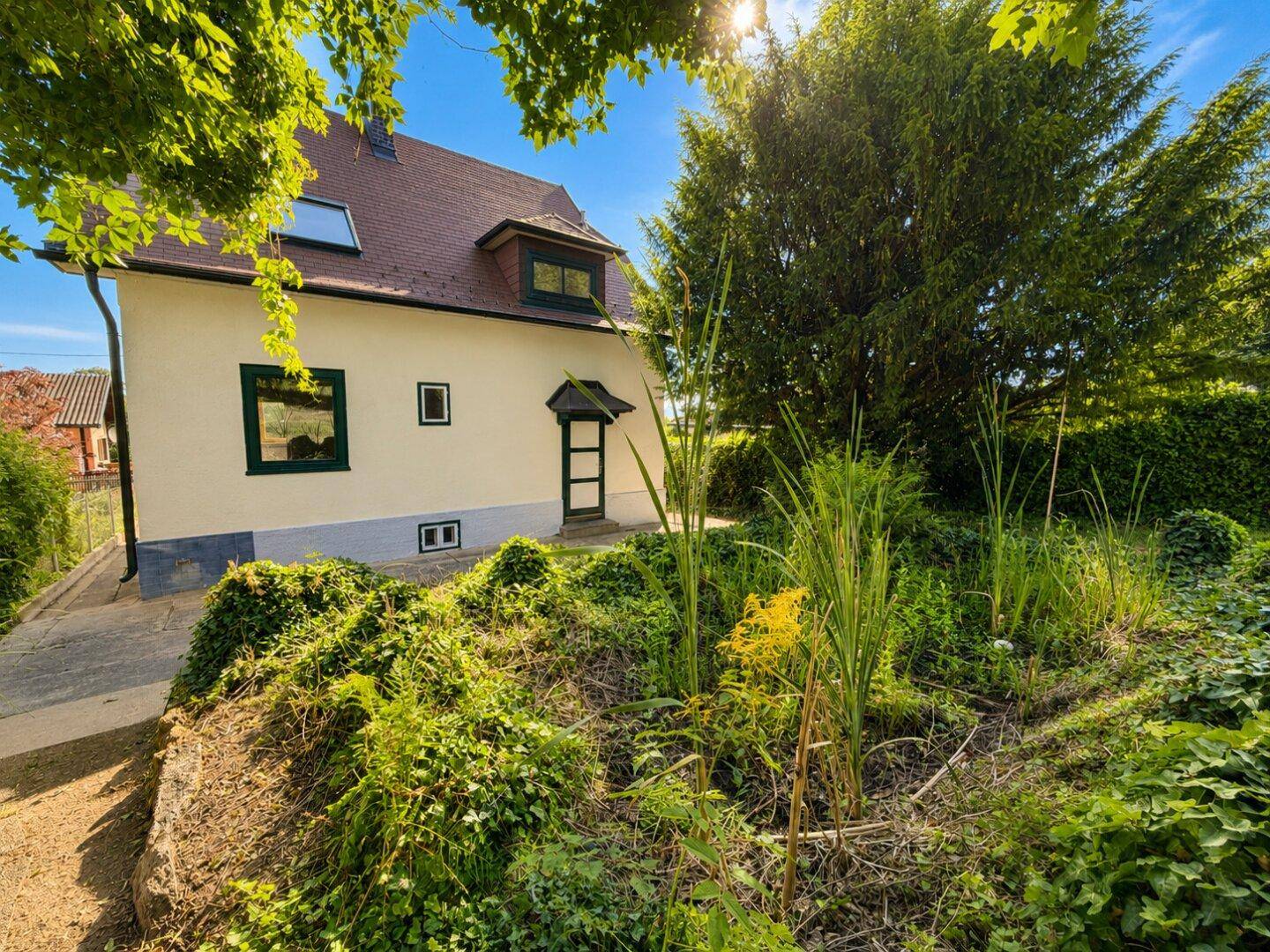 Charmantes Haus mit Satteldach und gepflegtem Garten unter strahlend blauem Himmel.