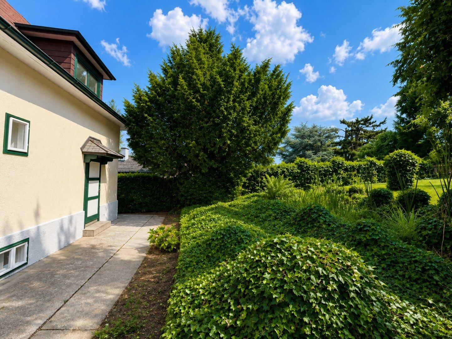 Seitenansicht des Hauses mit gepflastertem Weg und sorgfältig angelegtem Gartenbereich.