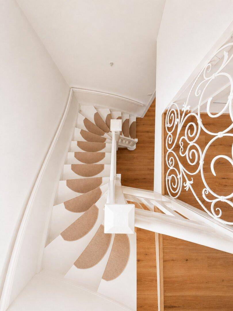Elegante Wendeltreppe mit Teppichläufern und kunstvollem Geländer.
