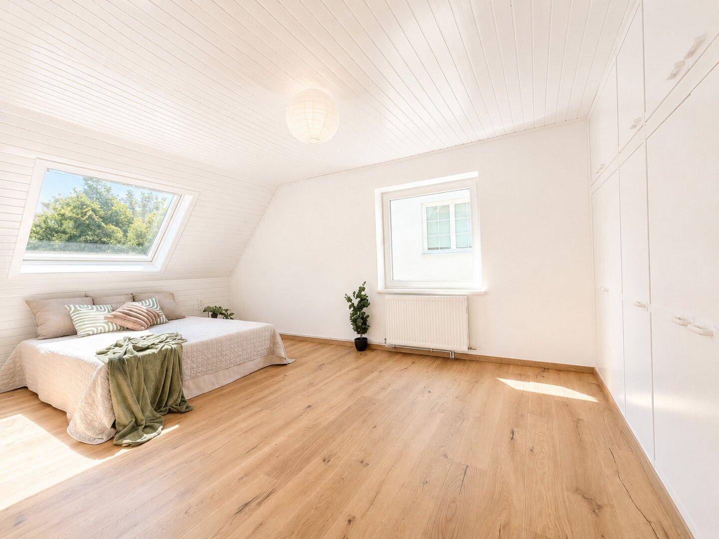Schlafzimmer im Dachgeschoss mit Holzboden, Einbauschränken und viel Tageslicht.