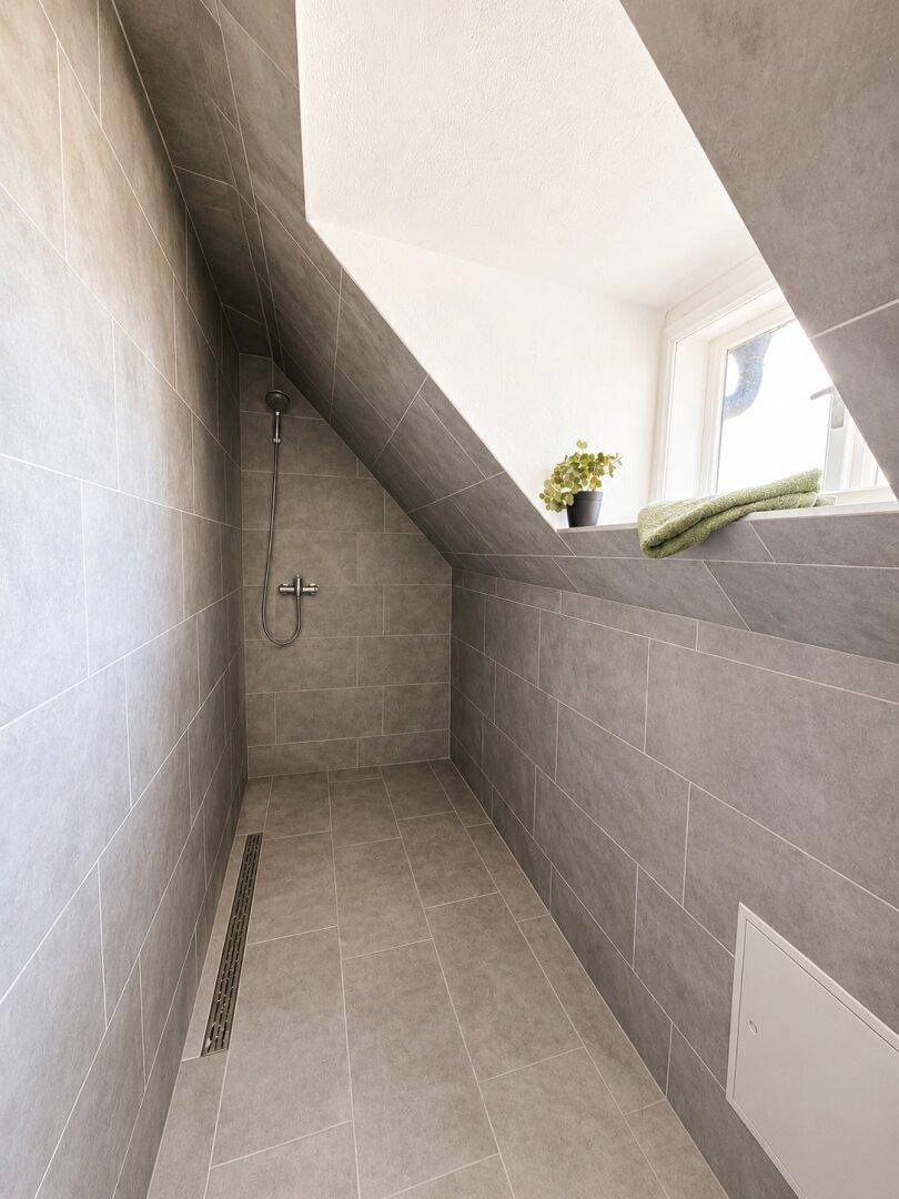 Moderne begehbare Dusche im Dachgeschoss mit grauen Fliesen und Dachschräge.