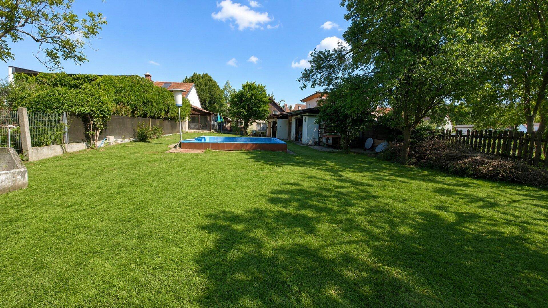 Weitläufiger Garten mit Rasenfläche, einem kleinen Pool und altem Baumbestand, umgeben von Wohnhäusern.