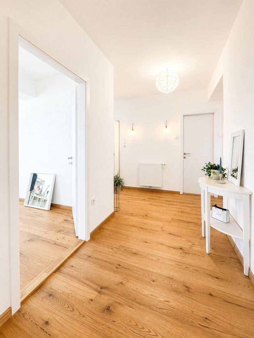 Heller Flur mit Holzboden und weißer Einrichtung, der zu weiteren Räumen führt.