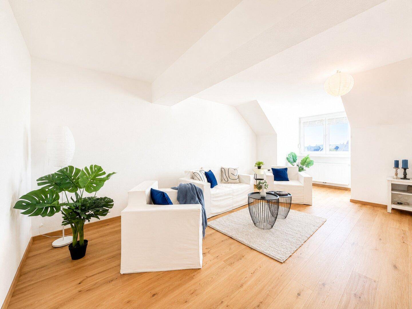 Lichtdurchflutetes Wohnzimmer mit Holzboden, weißen Möbeln und dekorativen Pflanzen.