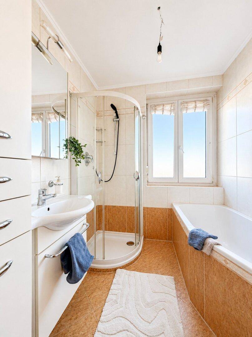 Badezimmer mit Badewanne, Duschkabine, Waschbecken und Fenster für Tageslicht.