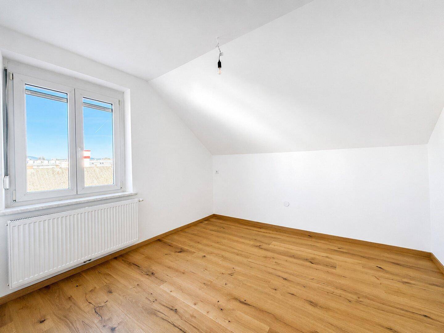 Geräumiges Schlafzimmer im Dachgeschoss mit Holzboden und viel Tageslicht durch das Fenster.