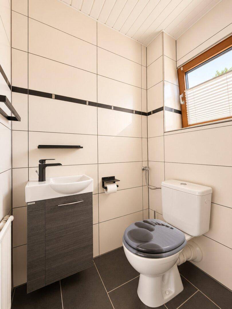 Funktionale Gästetoilette mit modernem Waschbecken, WC und Fenster.