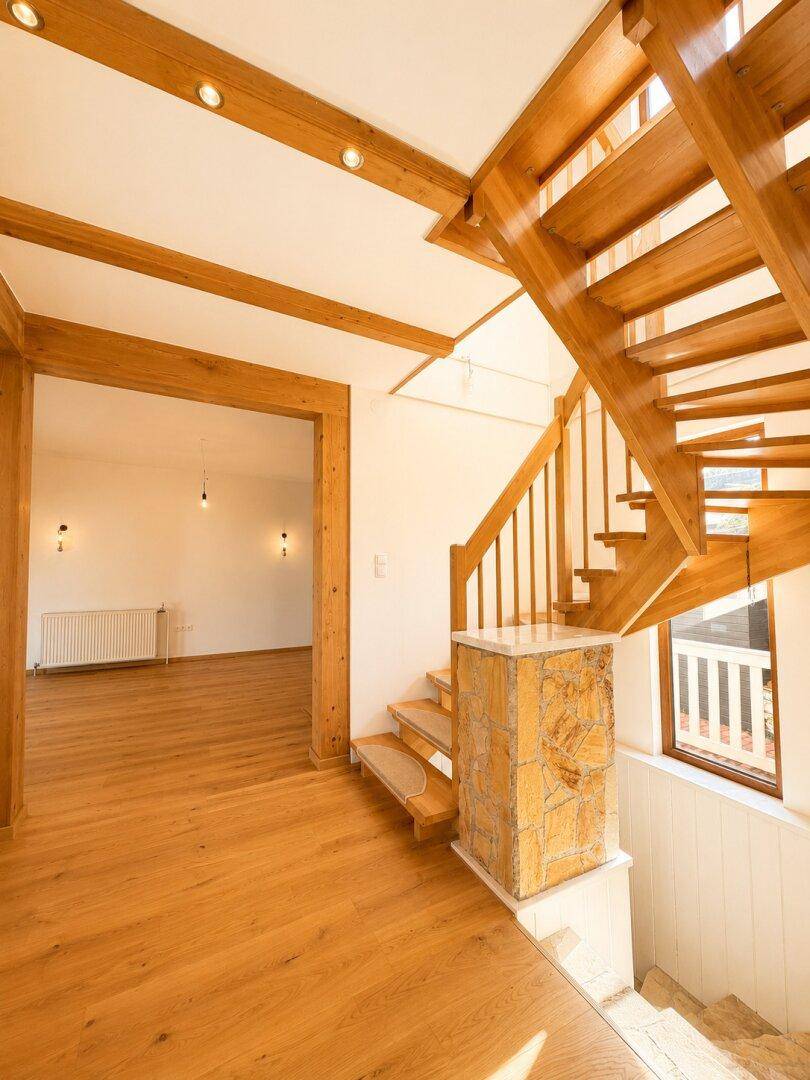 Elegante Holztreppe mit Steinakzenten und hellem Parkettboden im Eingangsbereich.