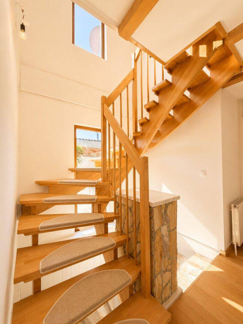 Geschwungene Holztreppe mit Teppichstufen und Fenster für natürliches Licht.
