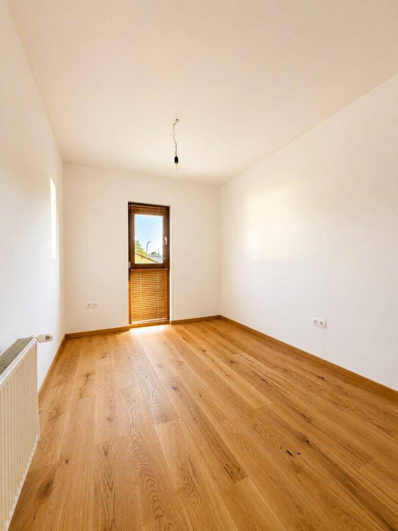 Geräumiges Zimmer mit Holzboden und Heizkörper, bietet viel natürliches Licht durch das Fenster.