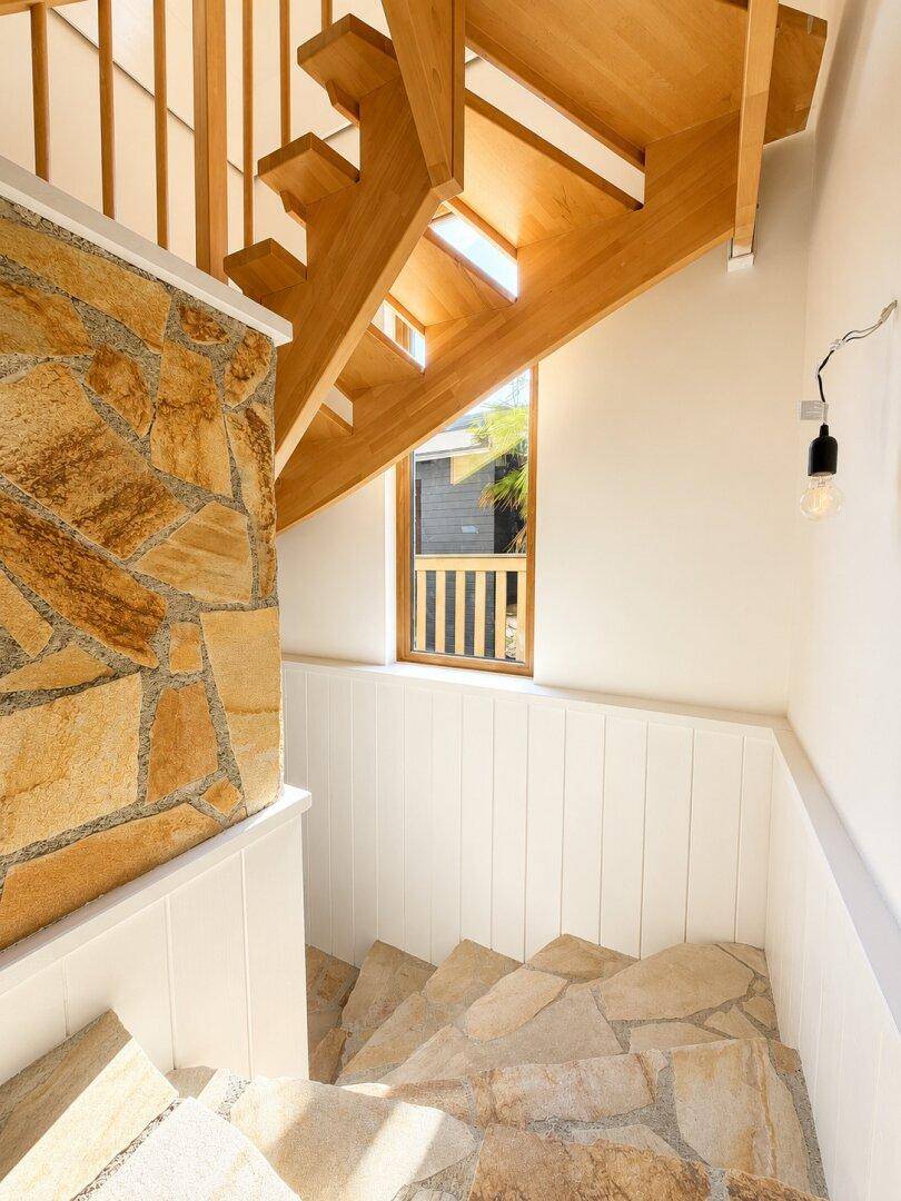 Treppenhaus mit Natursteinfliesen und Holztreppe, beleuchtet durch ein Fenster.