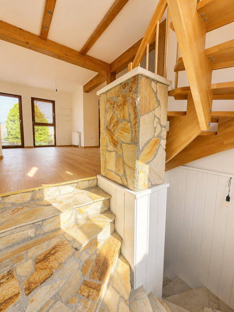 Eingangsbereich mit Natursteintreppe und sichtbaren Holzbalken, führt zu einem offenen Wohnbereich.