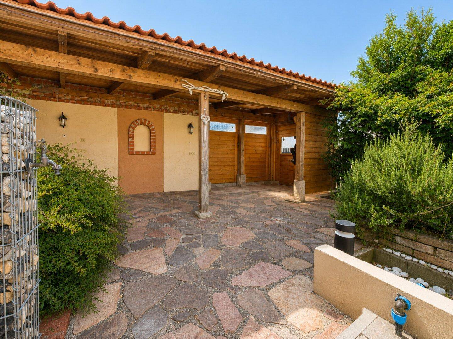 Geräumiger überdachter Außenbereich mit Holzdach und Steinboden, ideal als Carport oder Terrasse.