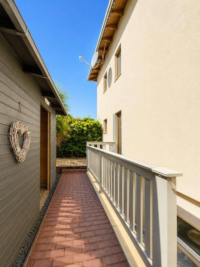 Schmaler Weg zwischen zwei Gebäuden mit Ziegelpflaster und Holzzaun.