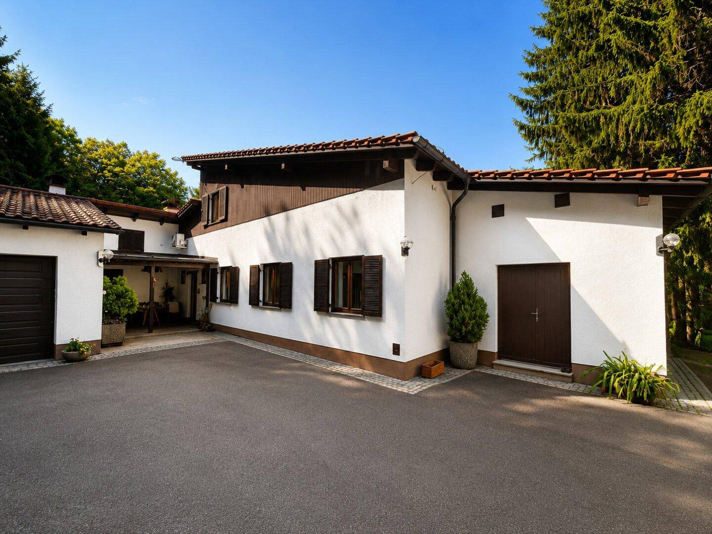 Ansicht des Hauses mit weißer Fassade, braunen Fensterläden und einer Zufahrt zur Garage.