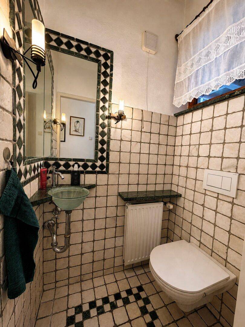 Kleines WC mit gemusterten Fliesen, wandhängender Toilette und einem kleinen Waschbecken.