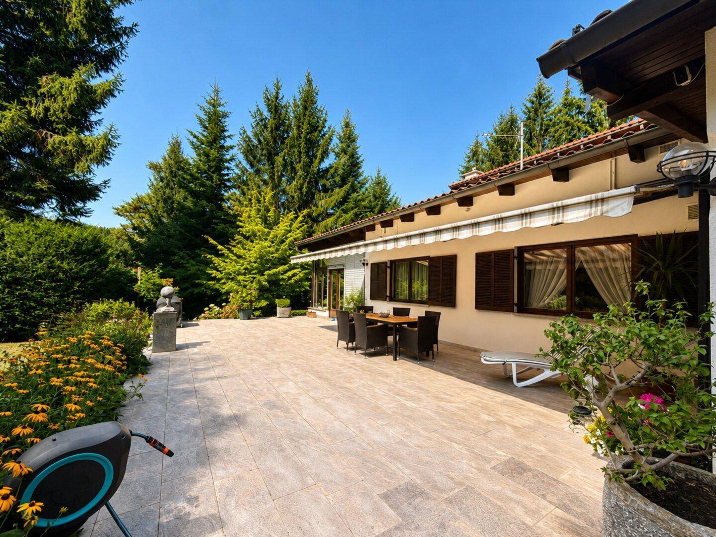 Weitläufige geflieste Terrasse mit Gartenmöbeln und Blick auf den grünen Gartenbereich des Hauses.