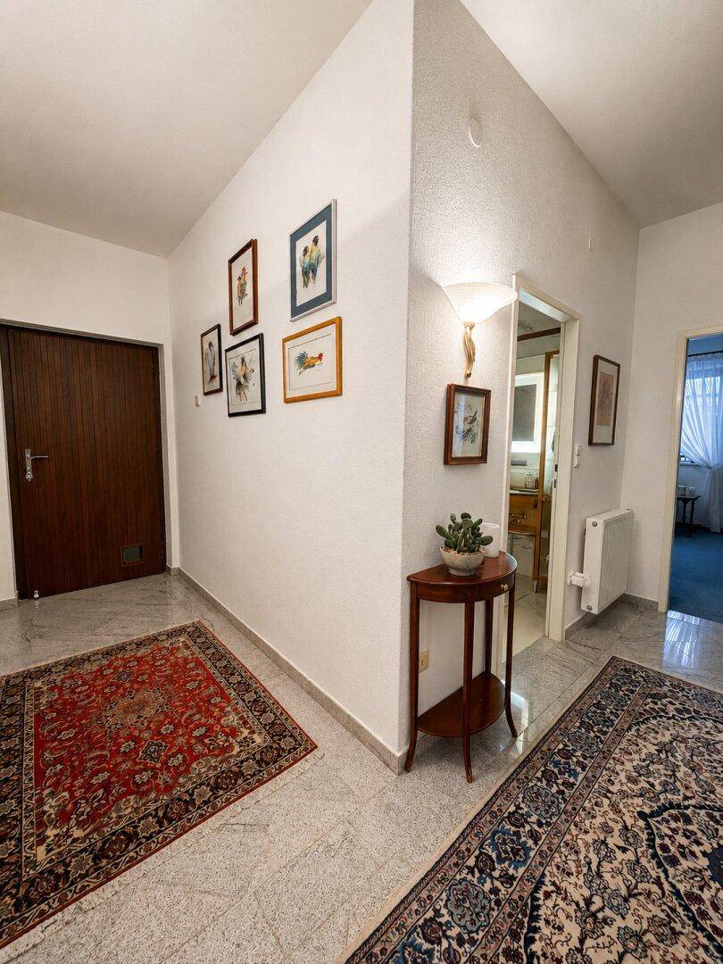 Heller Flur mit hellgrauem Fliesenboden, traditionellen Teppichen und gerahmten Bildern an der Wand.